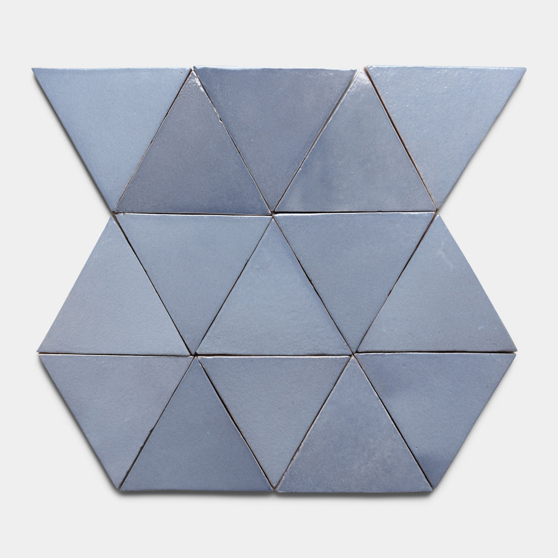 Twelve blue Pedregal Triangle tiles by Zia Tile are arranged in a geometric pattern—two rows of four triangles between two rows of two inverted triangles—set against a light grey background.