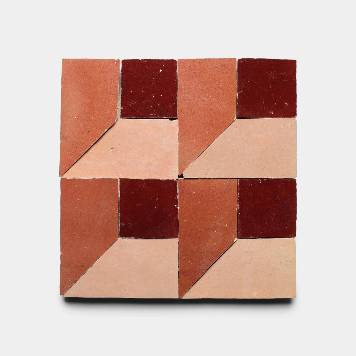 The Perpetual Check 3, Sample by Zia Tile is a handmade square tile with a geometric pattern of four smaller squares in dark red, medium red, and light beige, creating a 3D cube effect on a crisp white background.