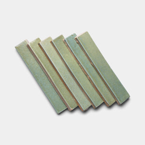 Six Peyote Mini Bar ceramic tiles by Zia Tile, rectangular and greenish with slightly textured surfaces, are arranged in a staggered, overlapping pattern on a white background.