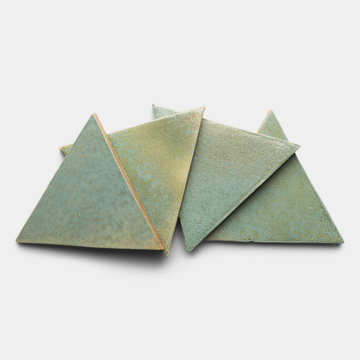 Four Peyote Triangle tiles by Zia Tile, featuring greenish ceramic with textured surfaces, are stacked and overlapping on a plain white background.