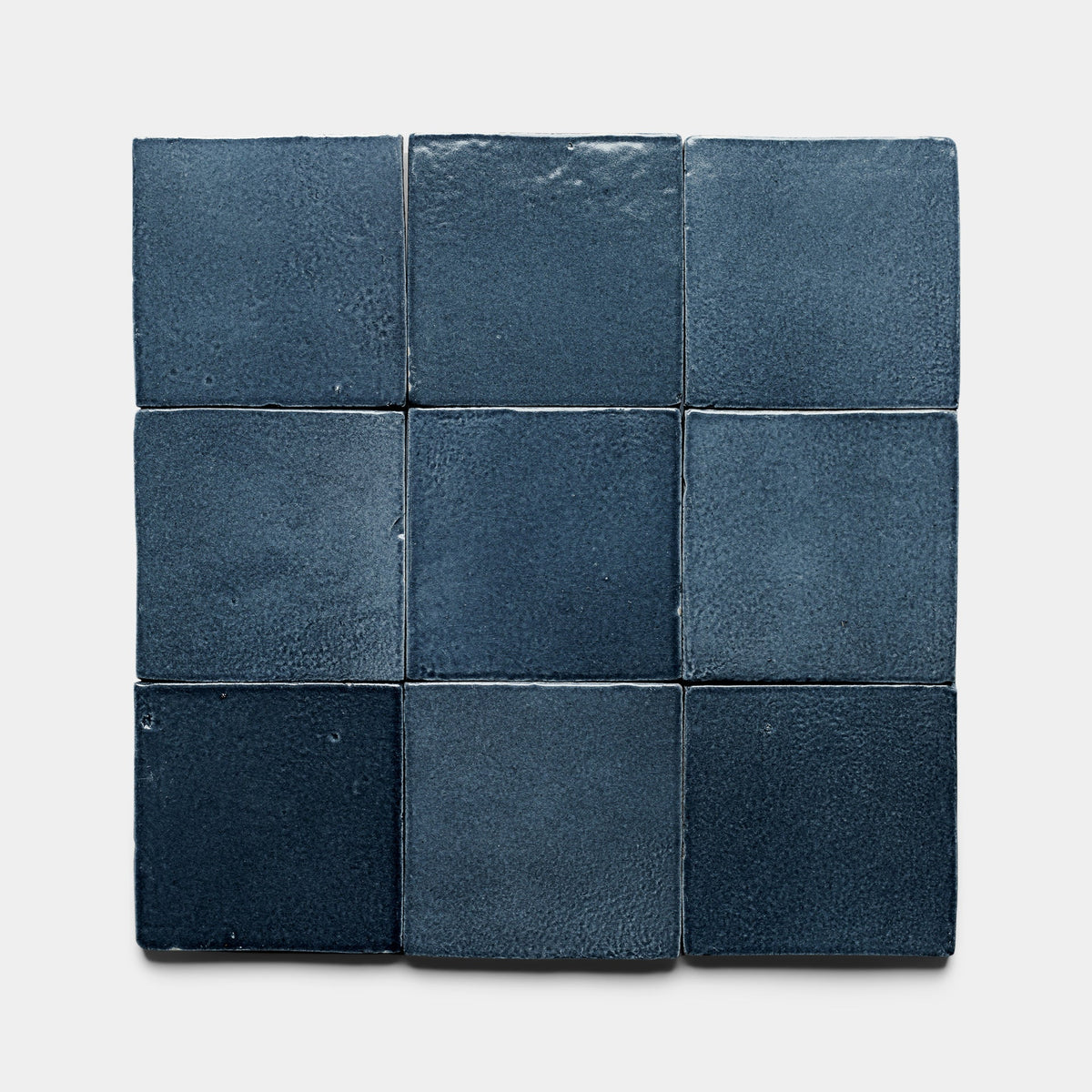 Nine Piedra 4x4 Square ceramic tile samples by Zia Tile, in dark blue with a matte, subtly textured surface and slight color variations, are arranged in a 3-by-3 grid on a light background.