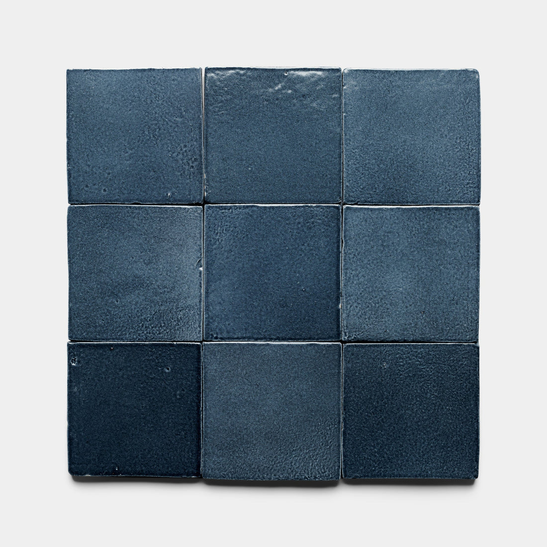 Nine Piedra 4x4 Square tiles by Zia Tile, dark blue with a matte, slightly textured surface and subtle shade variations, are arranged in a 3x3 grid on a light background, reflecting the handcrafted look of San Miguel de Allende Cotto.