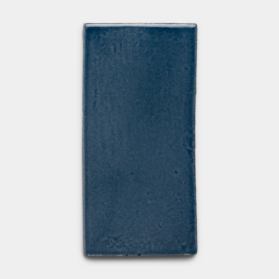 The Piedra 4x8 Rectangle by Zia Tile is a glossy ceramic tile in deep navy blue, displayed against a plain light gray background.