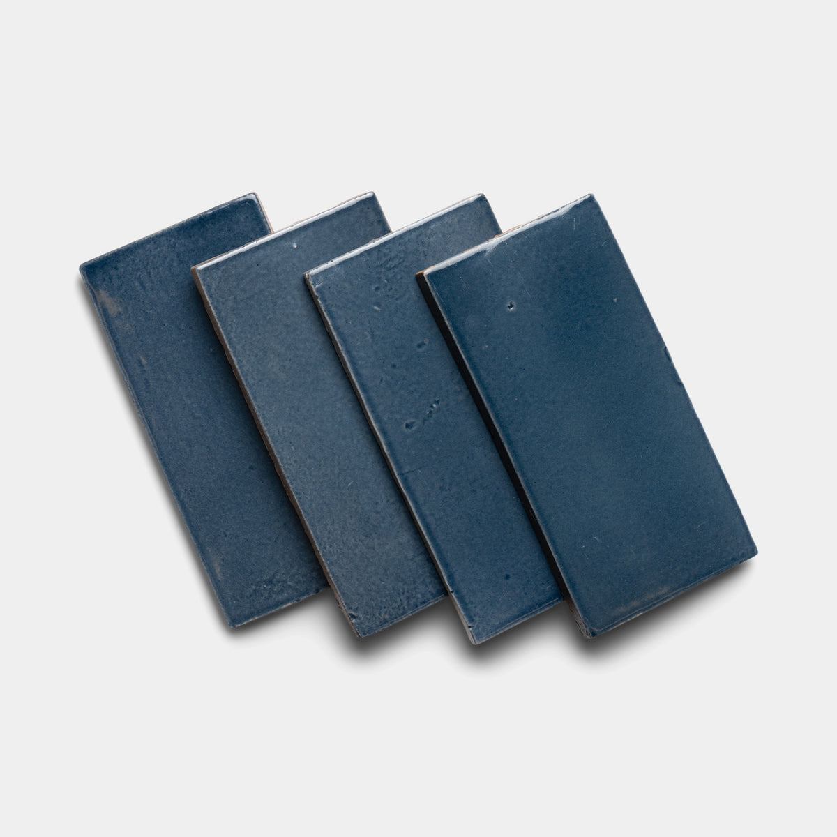 Four glossy Piedra 4x8 Rectangle ceramic tiles by Zia Tile are arranged in a slightly overlapping, fanned-out pattern on a white background.