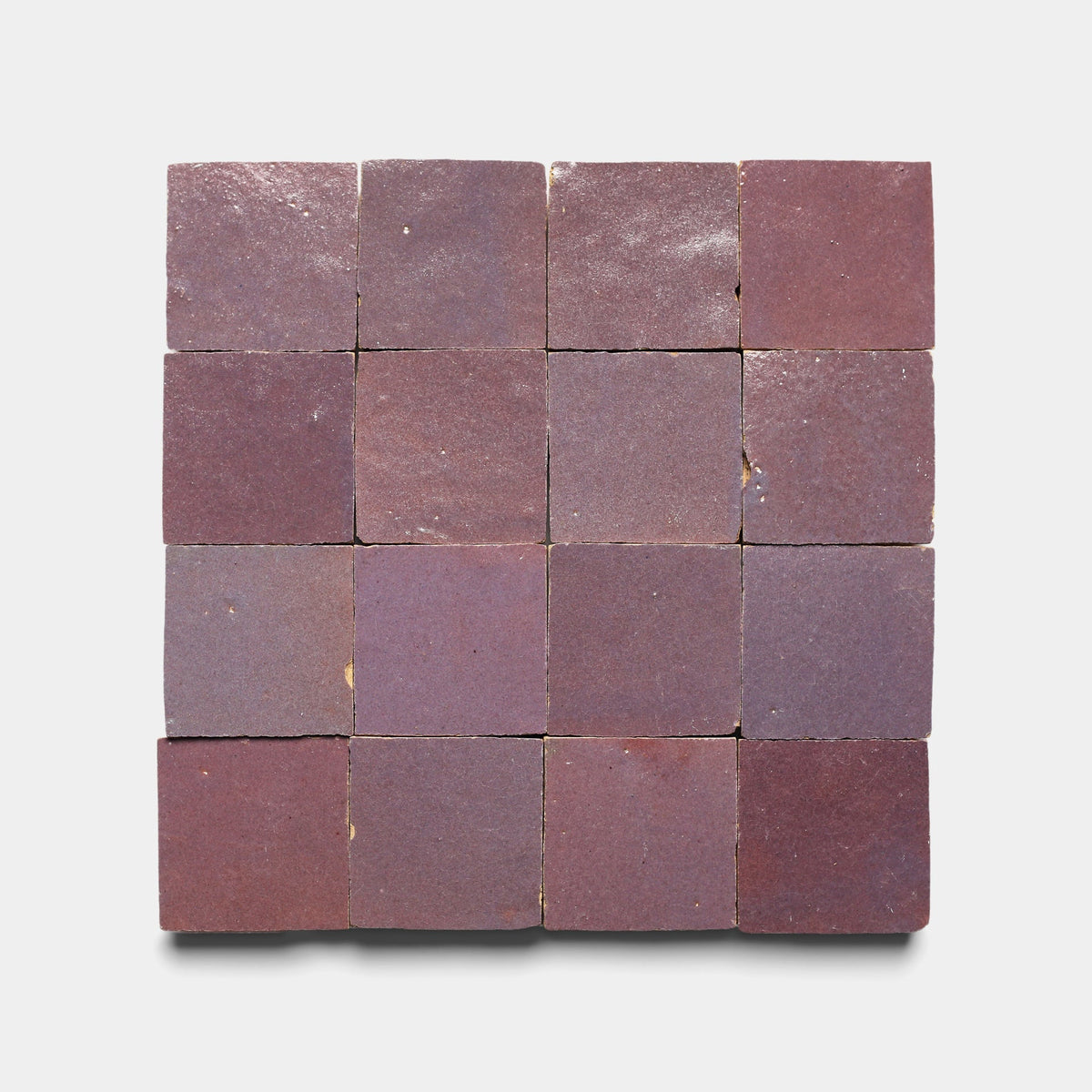 Sixteen Plum 2x2 handmade tiles from Zia Tile arranged in a 4x4 grid on a white background. The matte, reddish-brown tiles display subtle color and texture variations that highlight their artisanal craftsmanship.