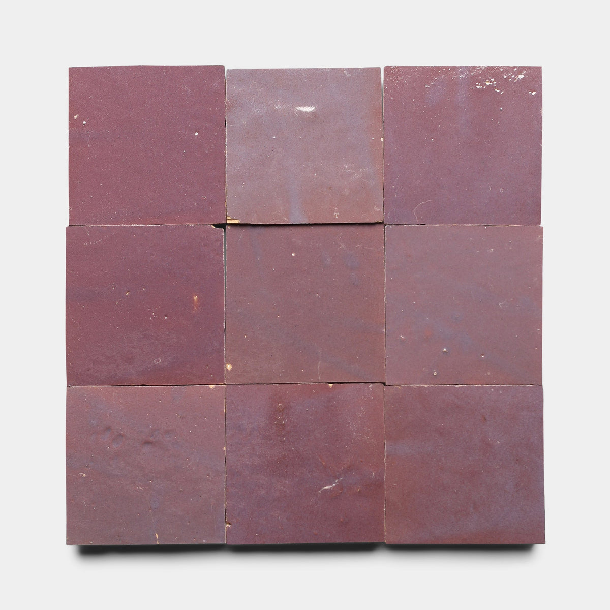 Nine Gypsum 4x4 matte, reddish-brown handmade tiles by Zia Tile are arranged in a three-by-three grid on a white background, showing subtle imperfections and slight color variations.