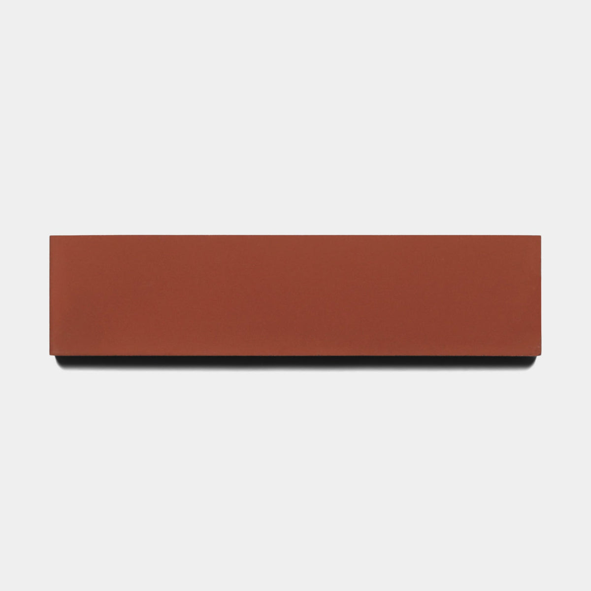 A rectangular Pompeii 2x8 Sample tile by Zia Tile in solid reddish-brown is centered on a plain white background, casting a small shadow below.