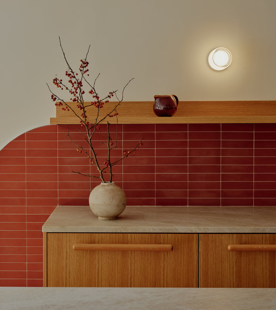 Kitchen counter with a red Zia Tile Pompeii 2x8 subway tile backsplash and a vase of berry branches.
