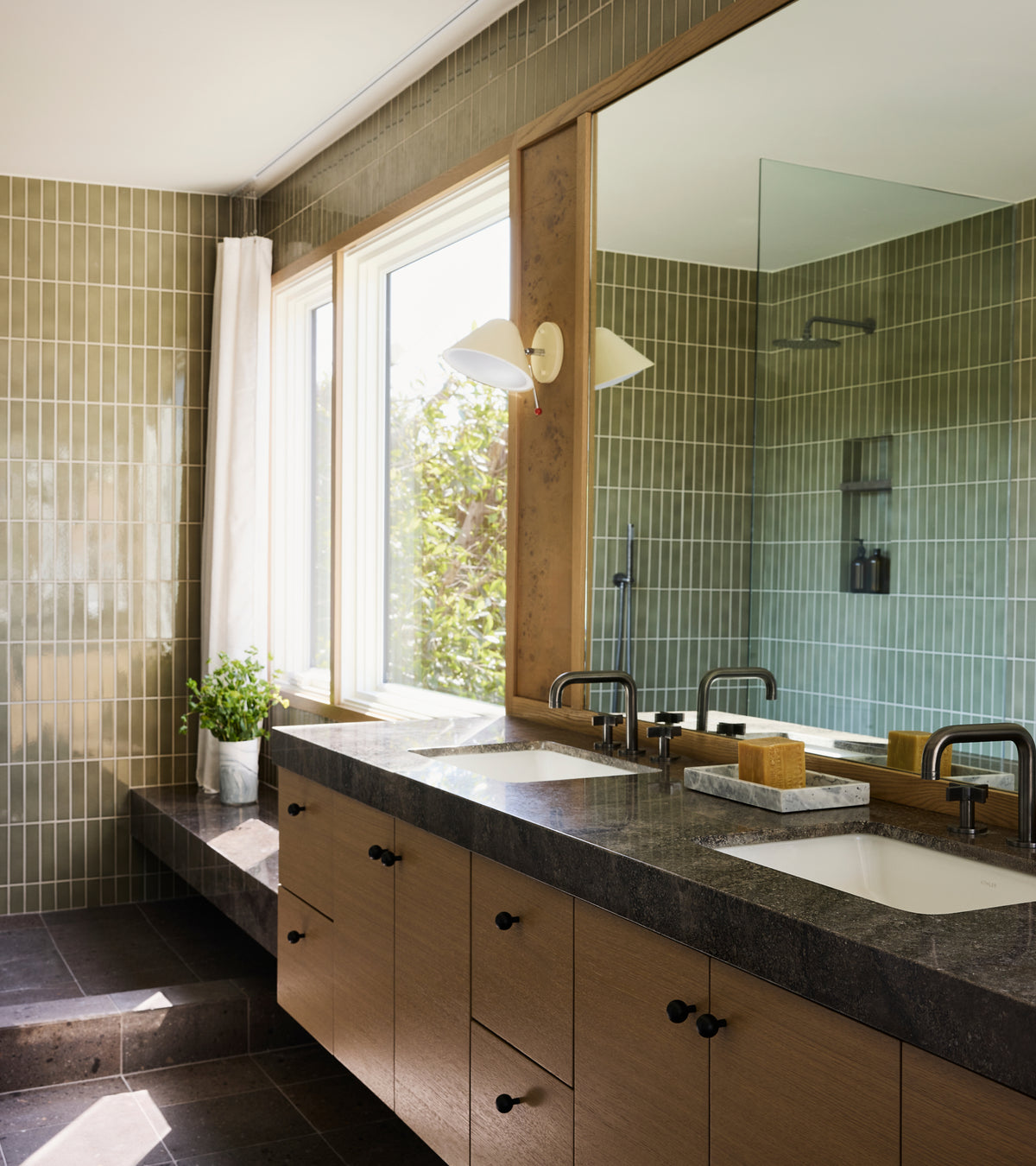 Double bathroom vanity with a dark stone countertop and light wood cabinets, set against walls covered in glossy, architectural-grade Ponderosa 2x8 ceramic tiles by Zia Tile.