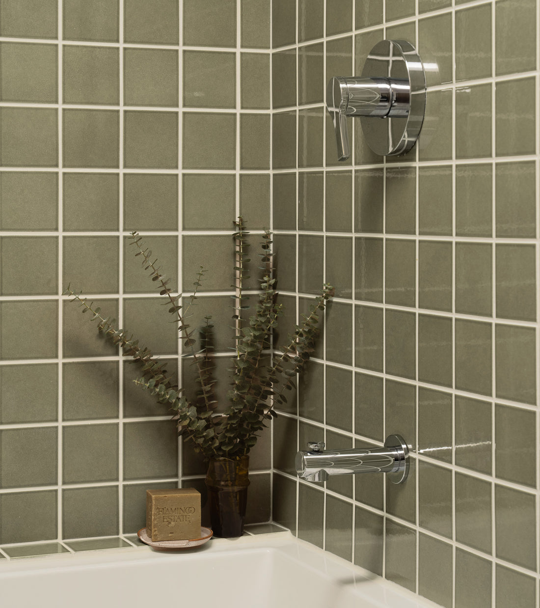 Square sage green Ponderosa 4x4 Zia Tile with white grout installed in a shower with chrome plumbing fixtures, a bar of soap, and a small plant.