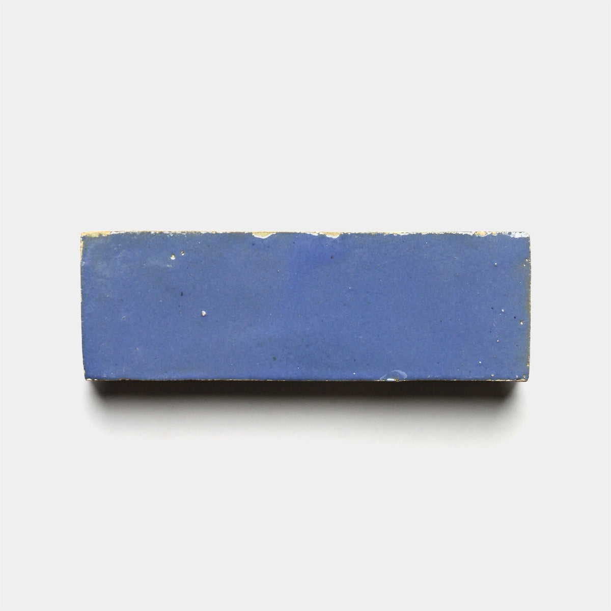 A Portuguese Blue 2x6 sample brick from Zia Tile, featuring slightly rough edges and a rectangular ceramic shape, is displayed on a plain white background.