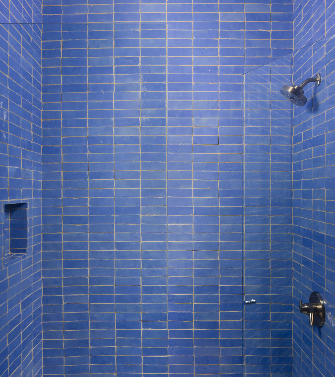 A shower stall featuring rectangular Portuguese Blue 2x6 Zellige tiles, a glass panel, and chrome fixtures.