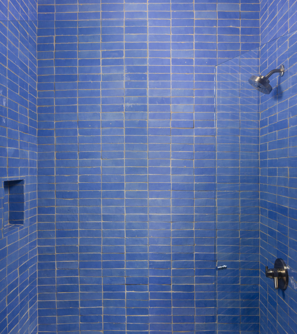 A shower stall featuring rectangular Portuguese Blue 2x6 Zellige tiles, a glass panel, and chrome fixtures.