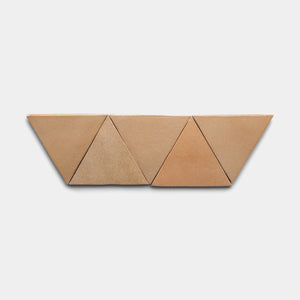 Four Posada Triangle tiles from Zia Tile, featuring tan and light brown ceramic in equilateral triangle shapes, are arranged in a zigzag row on a plain white background.