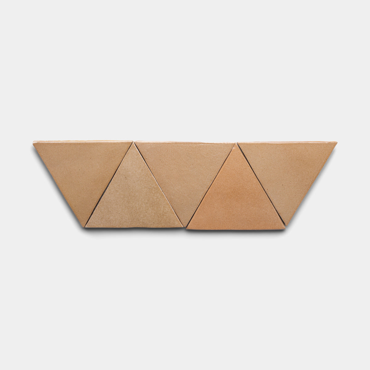 Four Posada Triangle tiles from Zia Tile, featuring tan and light brown ceramic in equilateral triangle shapes, are arranged in a zigzag row on a plain white background.