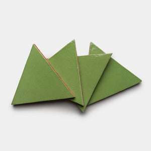 Four green Primavera Triangle tiles by Zia Tile, featuring a glossy finish and slightly rounded edges, overlap on a light gray background.