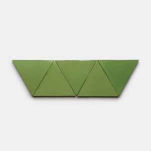 Four Zia Tile Primavera Triangle tiles, green and arranged in a row, create a symmetrical zigzag pattern against a plain white background.