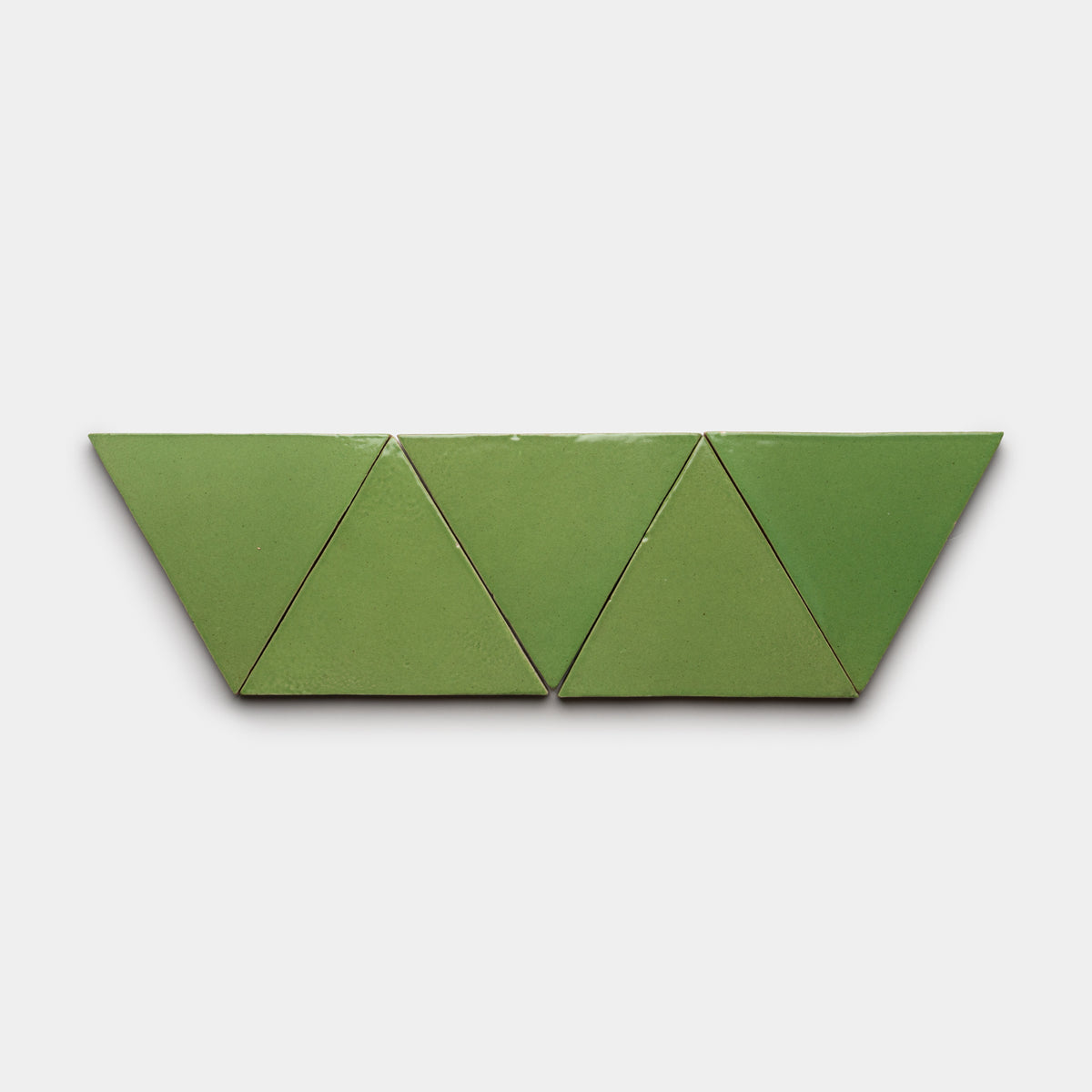 Four Zia Tile Primavera Triangle tiles, green and arranged in a row, create a symmetrical zigzag pattern against a plain white background.