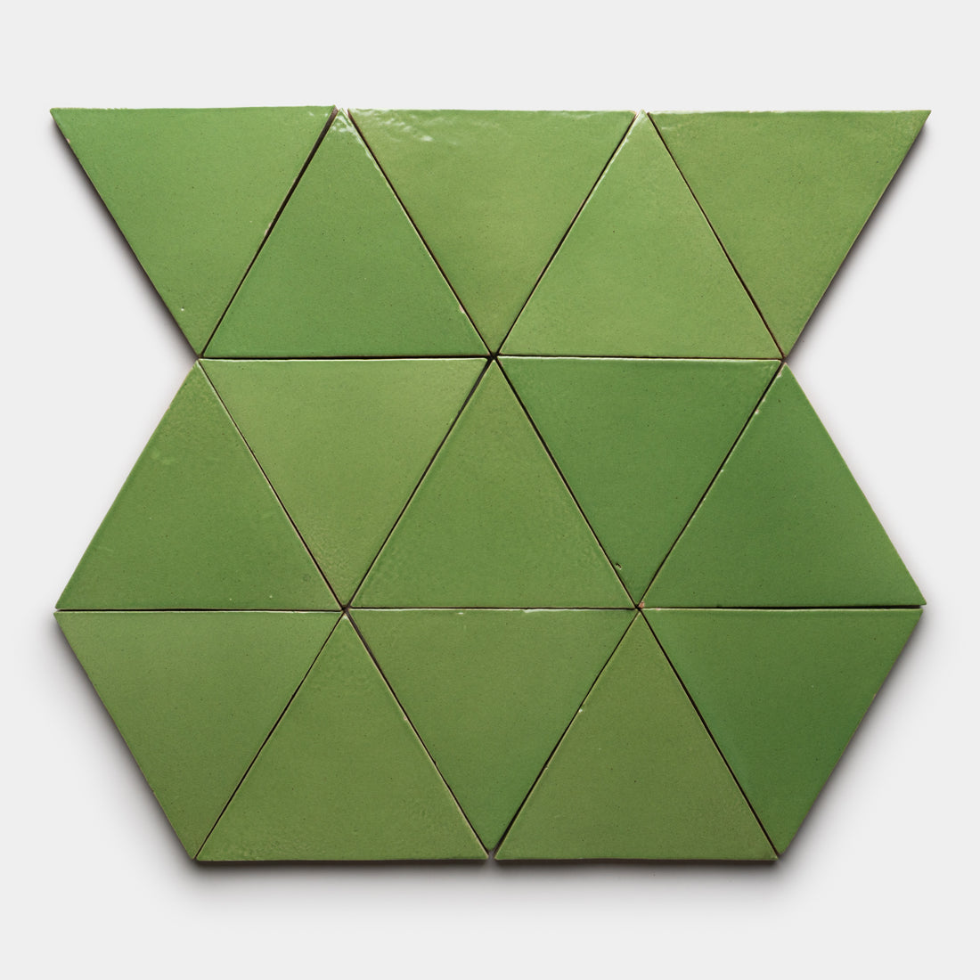 The Primavera Triangle tiles by Zia Tile feature green ceramic pieces arranged in hexagons and triangles on white, with slight shade variations that produce a subtle gradient pattern.