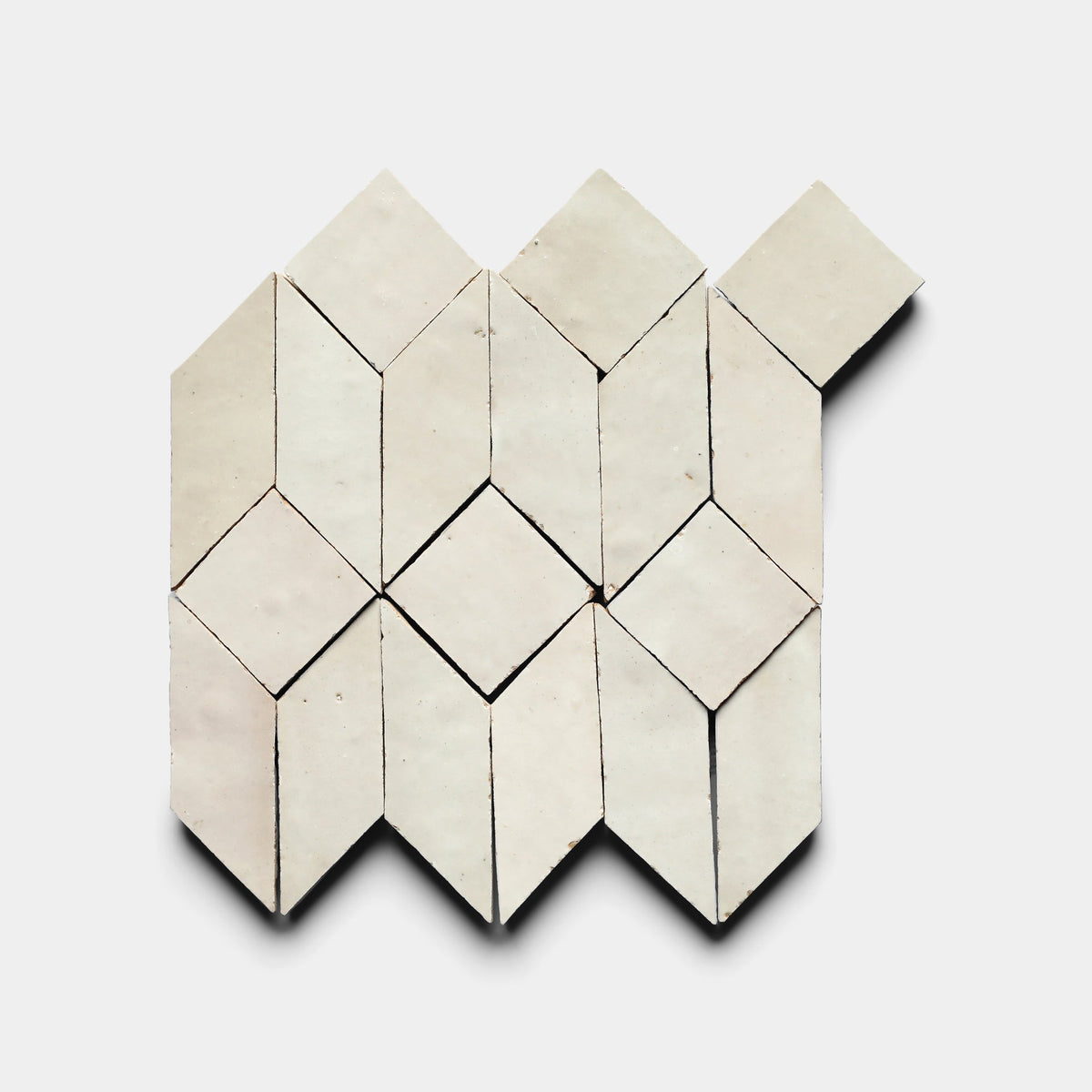 Prismatic 1, Sample by Zia Tile features white handmade tiles arranged in a repeating pattern of diamonds and parallelograms on a white background, with one top-right tile extending outward to break the symmetry.