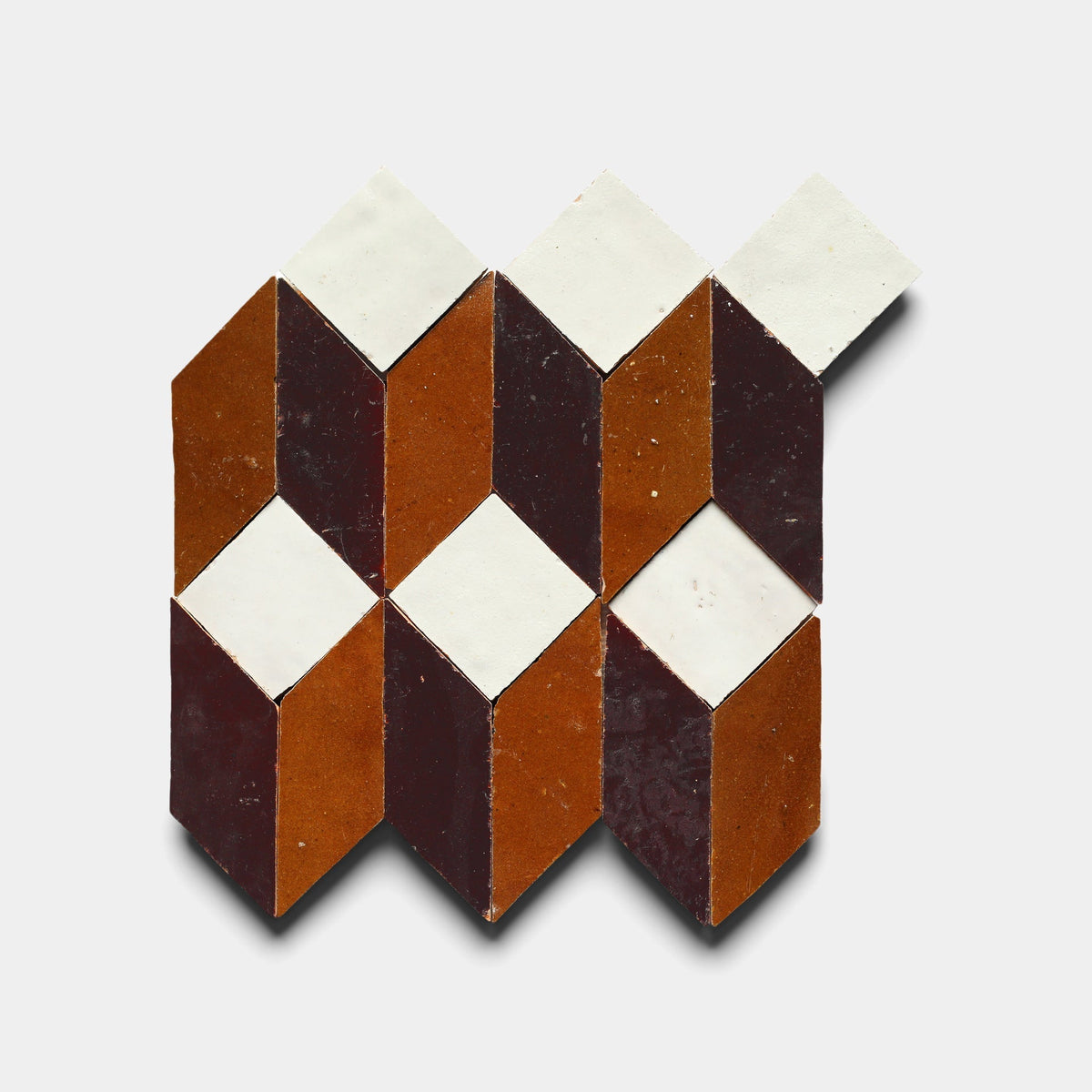 A geometric arrangement of red, brown, and white Prismatic 6 tiles by Zia Tile creates a 3D cube optical illusion on a white background.