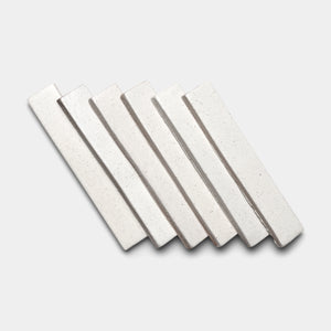 Six Puebla Mini Bar tiles by Zia Tile, featuring a rectangular shape and off-white ceramic with subtle speckles, are arranged diagonally and overlapping on a light gray background.