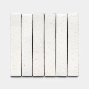 Six Puebla Mini Bar tiles by Zia Tile, rectangular and white with a smooth, slightly speckled finish, are arranged vertically in a neat row on a light gray background.