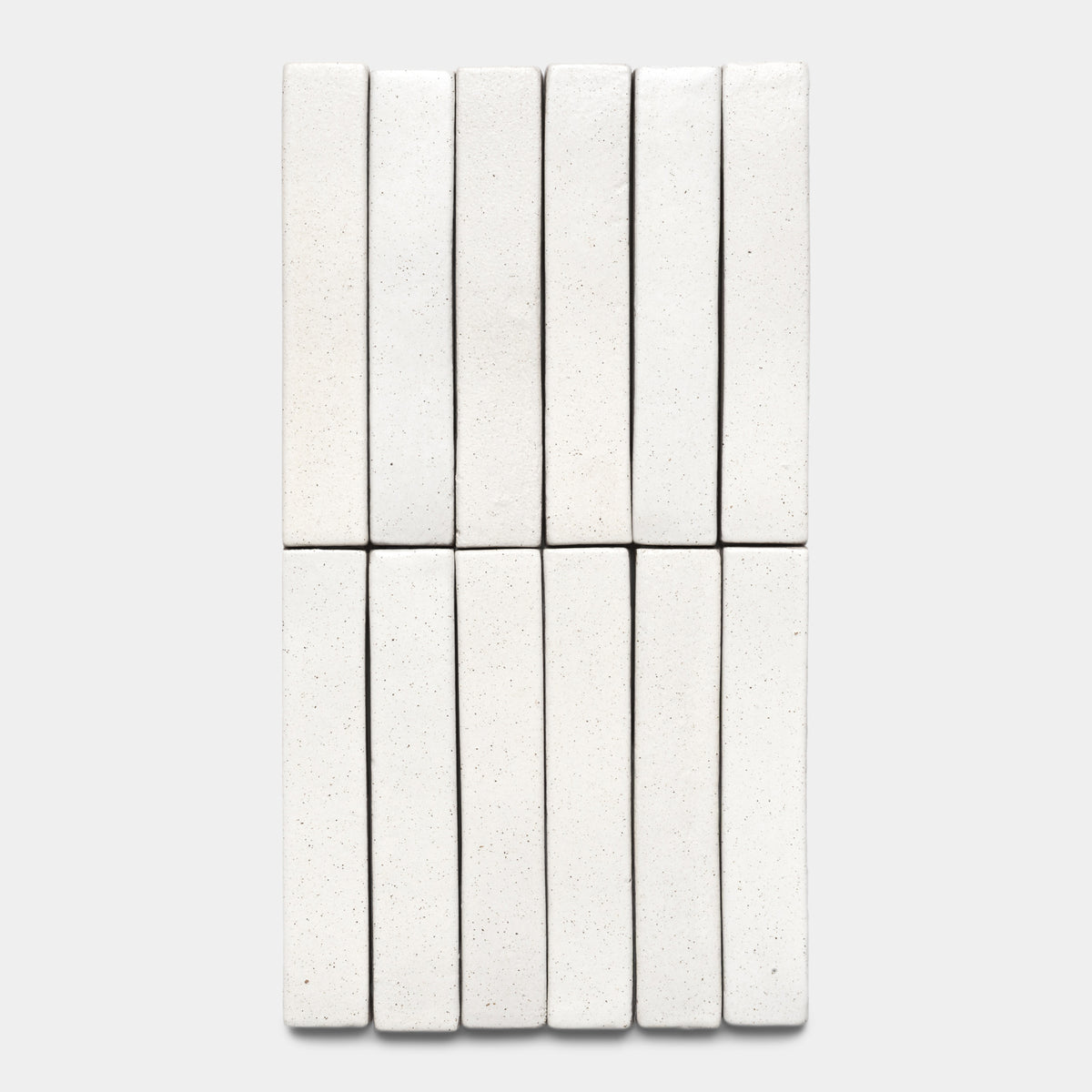 Twelve Puebla Mini Bar tiles by Zia Tile, rectangular and white with speckles, are neatly arranged in a grid on a plain light gray background.