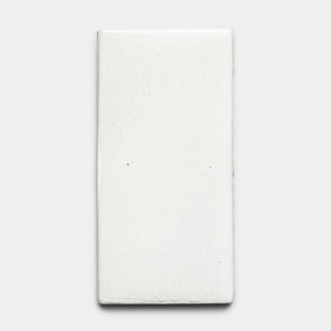 A rectangular, white Puebla 4x8 Rectangle ceramic tile by Zia Tile with a slightly uneven surface and subtle speckling, displayed against a plain light gray background.