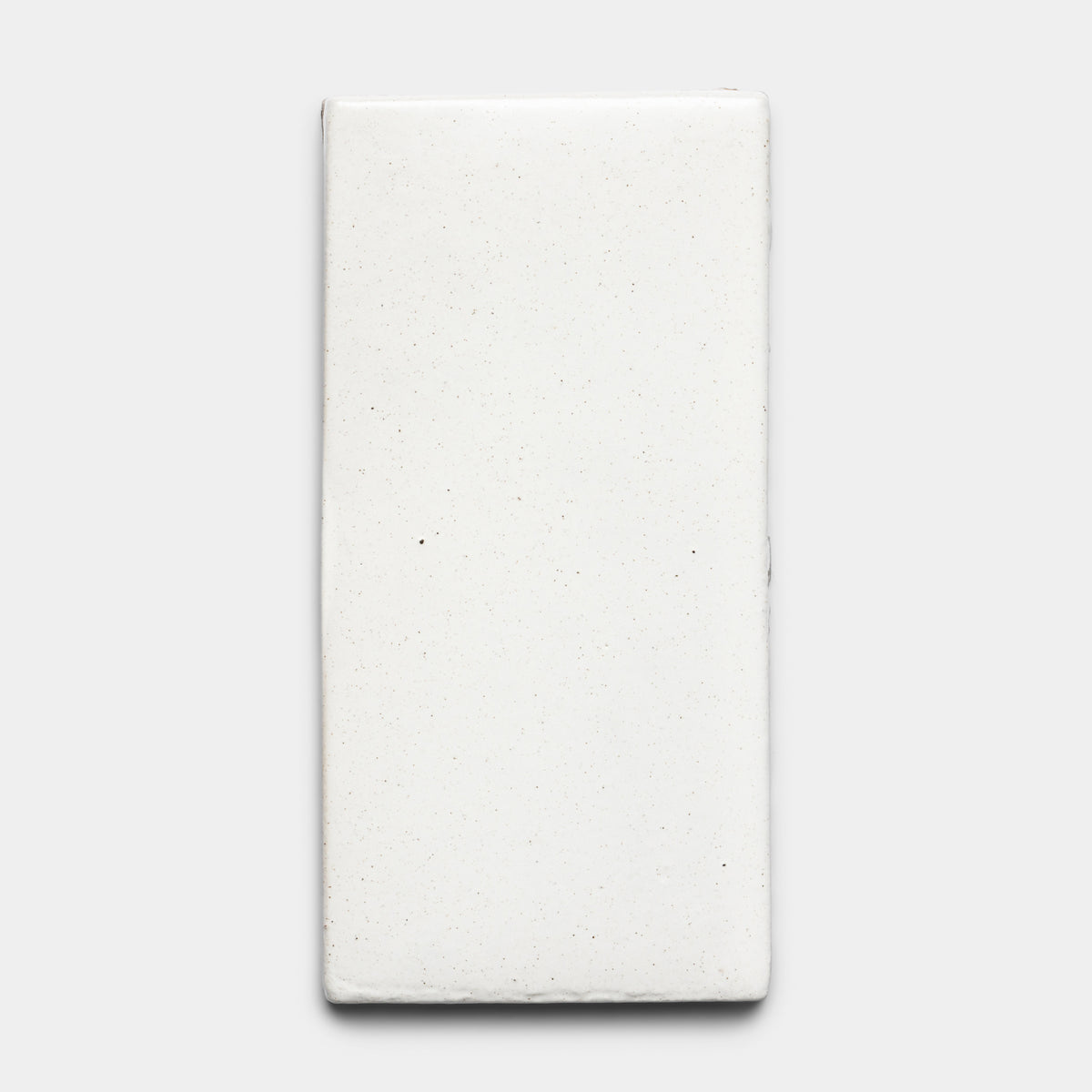 A rectangular, white Puebla 4x8 Rectangle ceramic tile by Zia Tile with a slightly uneven surface and subtle speckling, displayed against a plain light gray background.