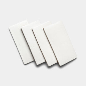 Four white rectangular ceramic tiles are arranged in an overlapping, slightly fanned pattern on a plain light gray background, highlighting the clean style of Zia Tile's Puebla 4x8 Rectangle.