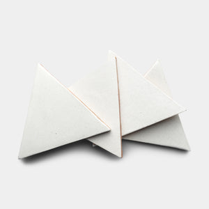 Four Puebla Triangle tiles by Zia Tile in white speckled ceramic overlap on a plain light gray background.