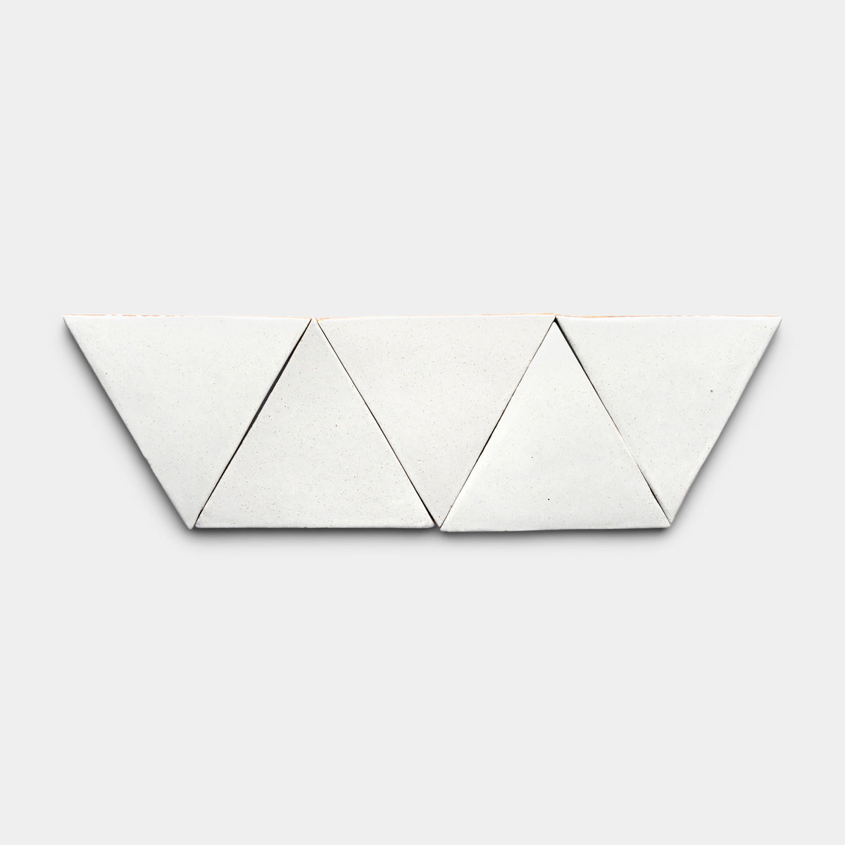 Four Puebla Triangle tiles by Zia Tile are arranged side by side on a light gray background, creating a striking horizontal geometric pattern.