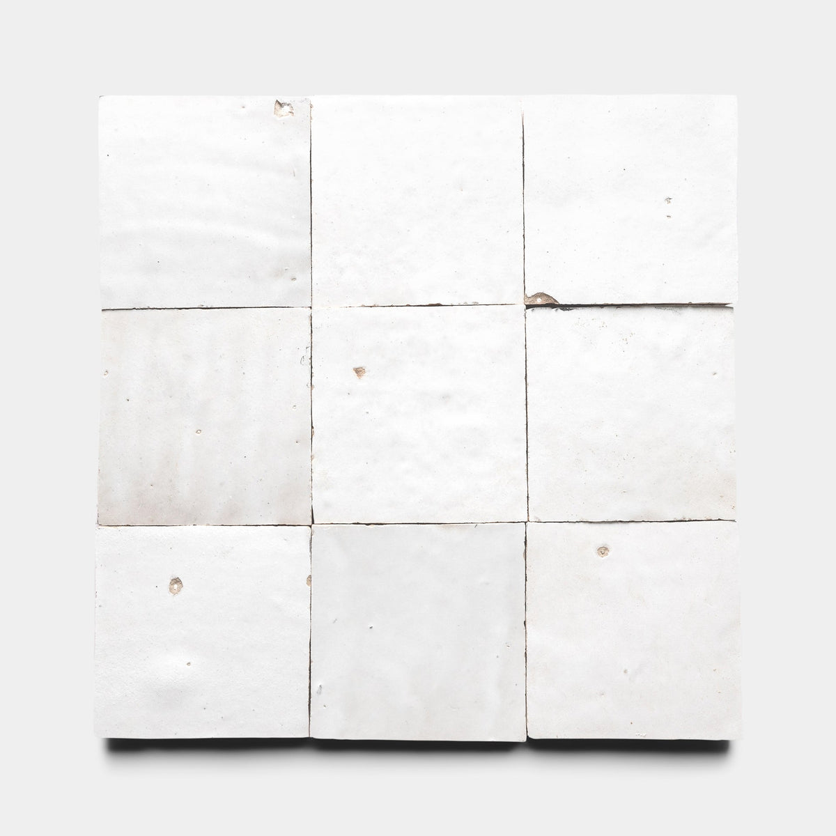 A square grid of nine Protea 4x4 ceramic tile samples by Zia Tile, each white with slight imperfections and chips, arranged on a plain light gray background.
