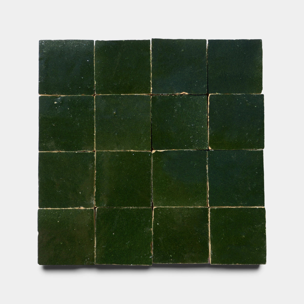 Sixteen Prairie Green 2x2 glossy handmade tiles by Zia Tile are arranged in a four-by-four grid on a light background. Each tile shows subtle shade and texture variations, with visible grout lines separating the dark green squares.