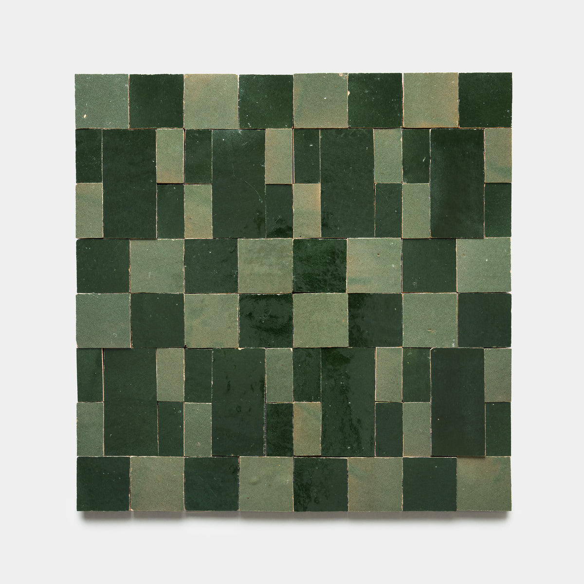 Souk 1 by Zia Tile features rectangular and square green tiles in varying shades, arranged in a geometric grid pattern on a light background, creating a symmetrical mosaic with alternating dark and light green tones.