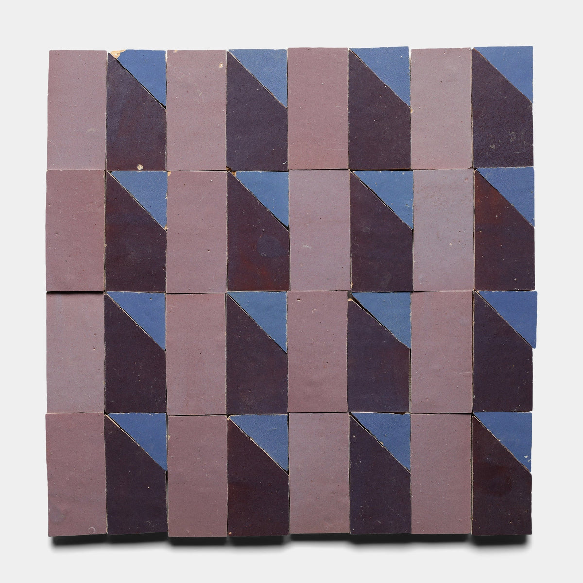 The Radian Inline 3 tile sample by Zia Tile features a square grid of handmade tiles, each split diagonally into dark purple and blue triangles, creating a repeating geometric pattern on a white background.