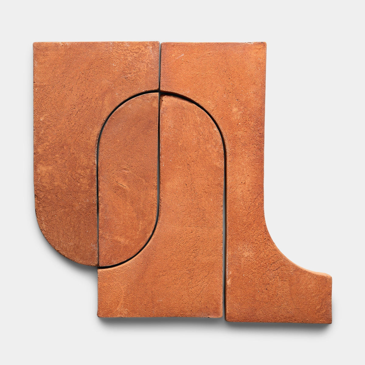 Three Durango + Red Clay samples by Zia Tile with smooth, reddish-brown surfaces are arranged in an abstract geometric pattern of curved and straight edges against a plain white background.