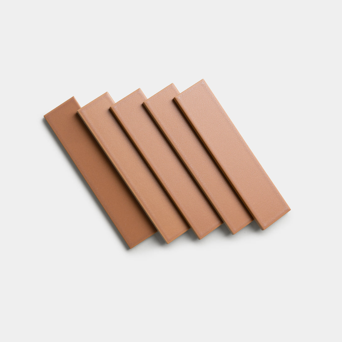 Five rectangular, light brown Rhubarb 2x8 tiles by Zia Tile are arranged diagonally and overlapping on a plain white background.