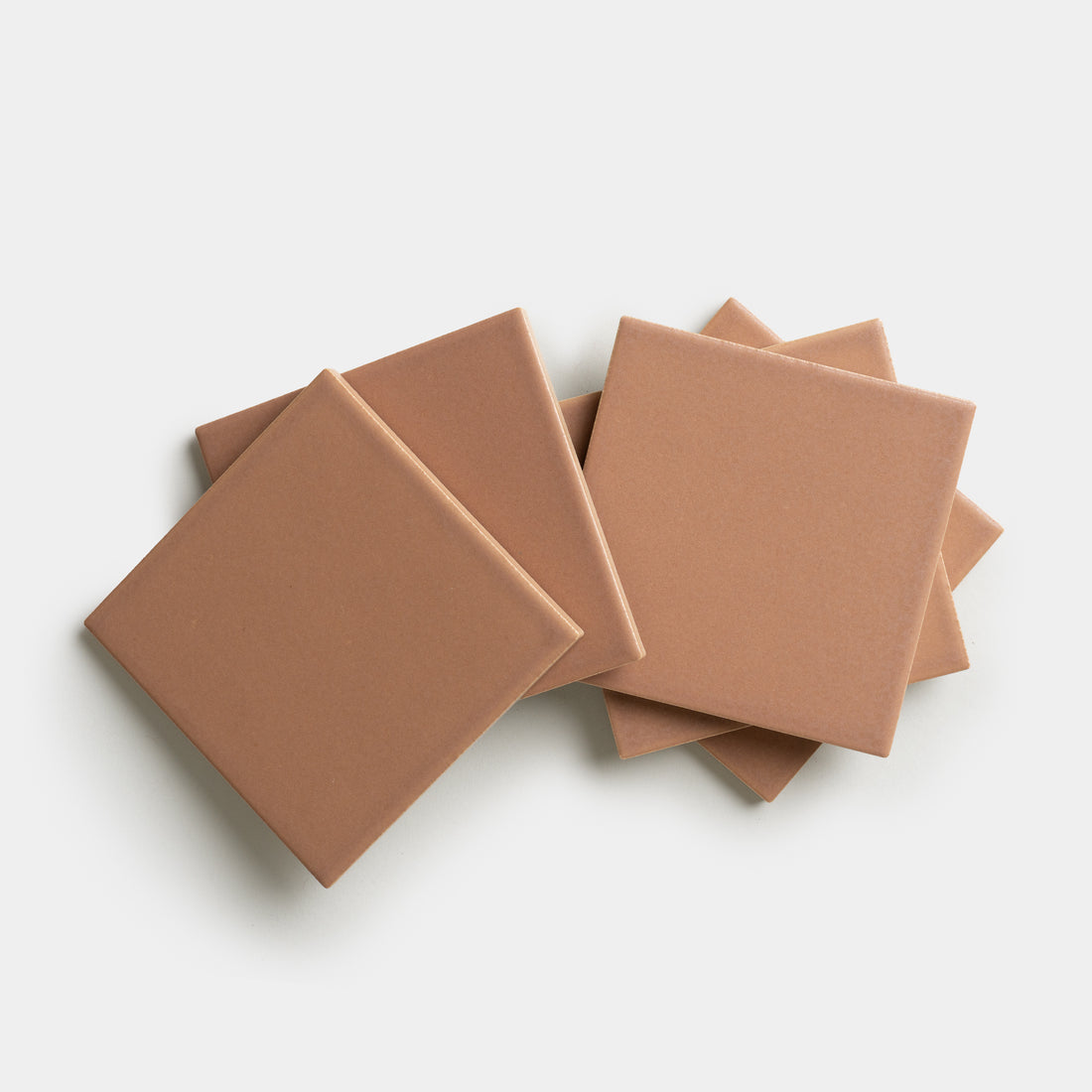 Five Rhubarb 4x4 ceramic tiles by Zia Tile, in a light brown shade, are stacked and slightly fanned out against a white background.