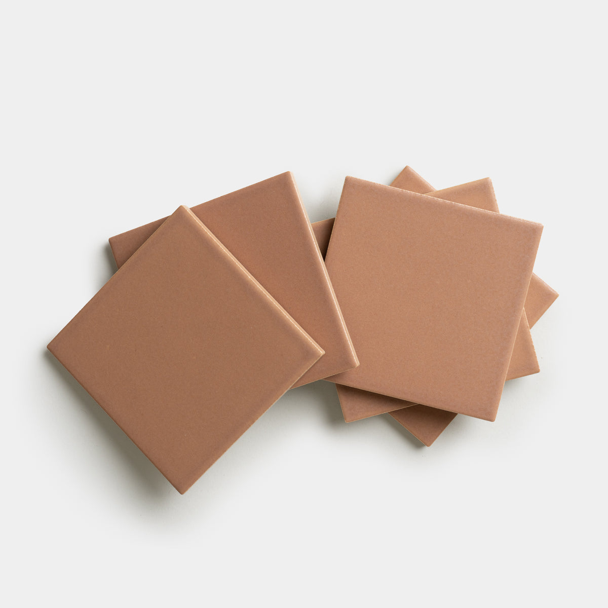 Five Rhubarb 4x4 ceramic tiles by Zia Tile, in a light brown shade, are stacked and slightly fanned out against a white background.