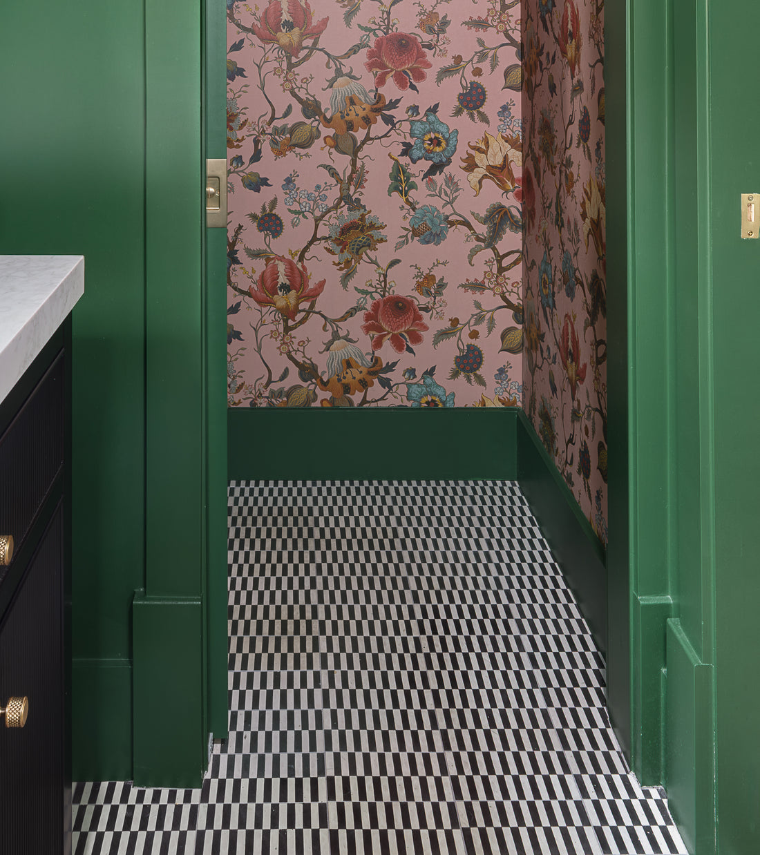 A hallway features green-trimmed doors, pink floral wallpaper, and a floor tiled with Zia Tile's Rialto Black 4x8. On the left, a marble countertop and dark cabinets are partly visible.