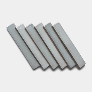 Six Roca Mini Bar tiles by Zia Tile, in light gray ceramic with a rectangular shape, are arranged diagonally in a staggered, overlapping pattern on a plain white background.