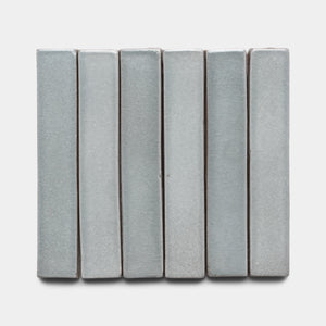 Six rectangular, vertical Roca Mini Bar tiles by Zia Tile in light gray are arranged side by side on a plain white background.