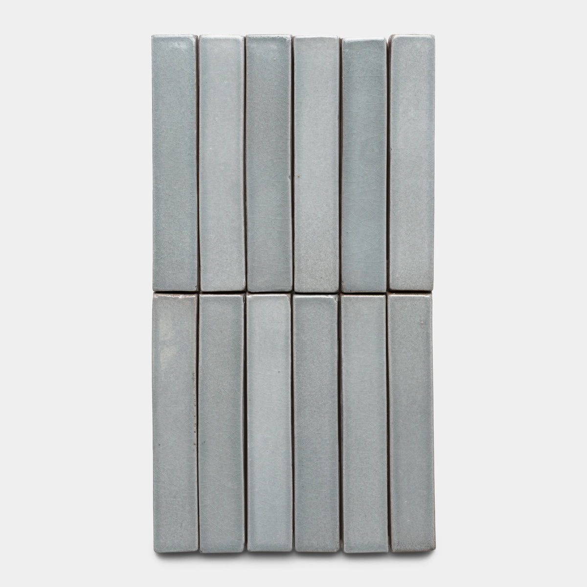 Twelve Roca Mini Bar tiles by Zia Tile in light gray are arranged vertically in a 4x3 grid on a plain white background.