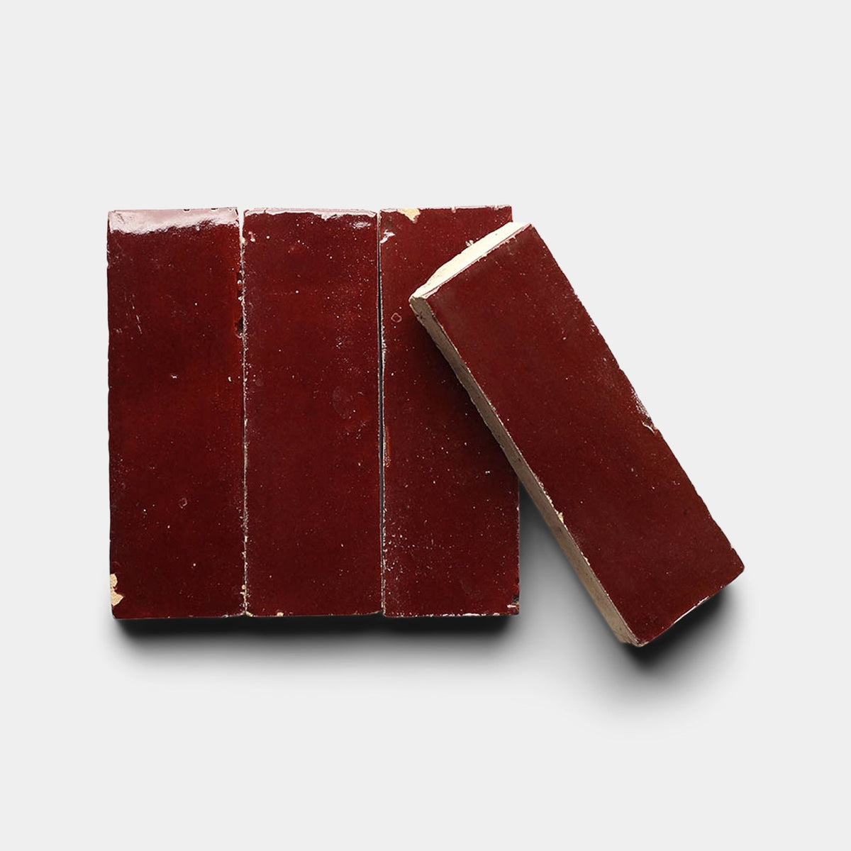 Four glossy, rectangular Rouge 2x6 samples by Zia Tile in dark red are arranged on a light background—three aligned side by side with one diagonally placed across them.