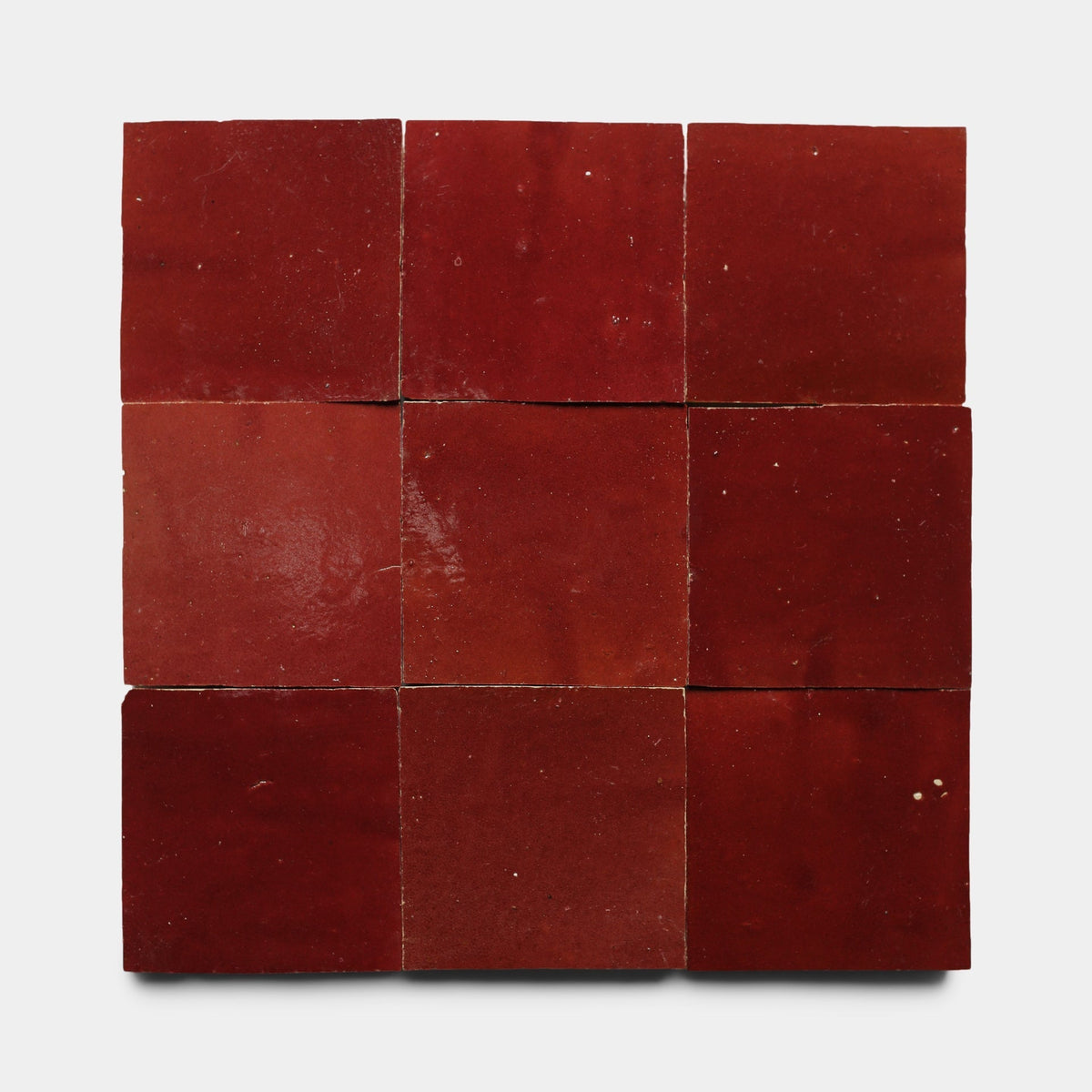 Nine glossy red Rouge 2x6 samples by Zia Tile are arranged in a 3x3 grid on a white background, each showing slight variations in shade, texture, and subtle surface imperfections.