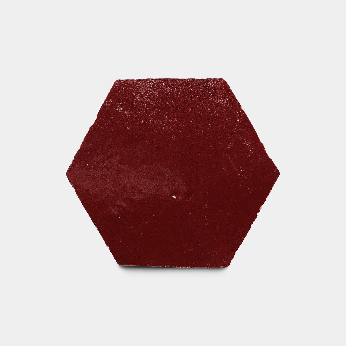 A single Rouge 2x6 sample tile by Zia Tile is displayed against a white background. The tile features a solid, dark red color, hexagonal shape, smooth surface with subtle texture, and sharp edges.