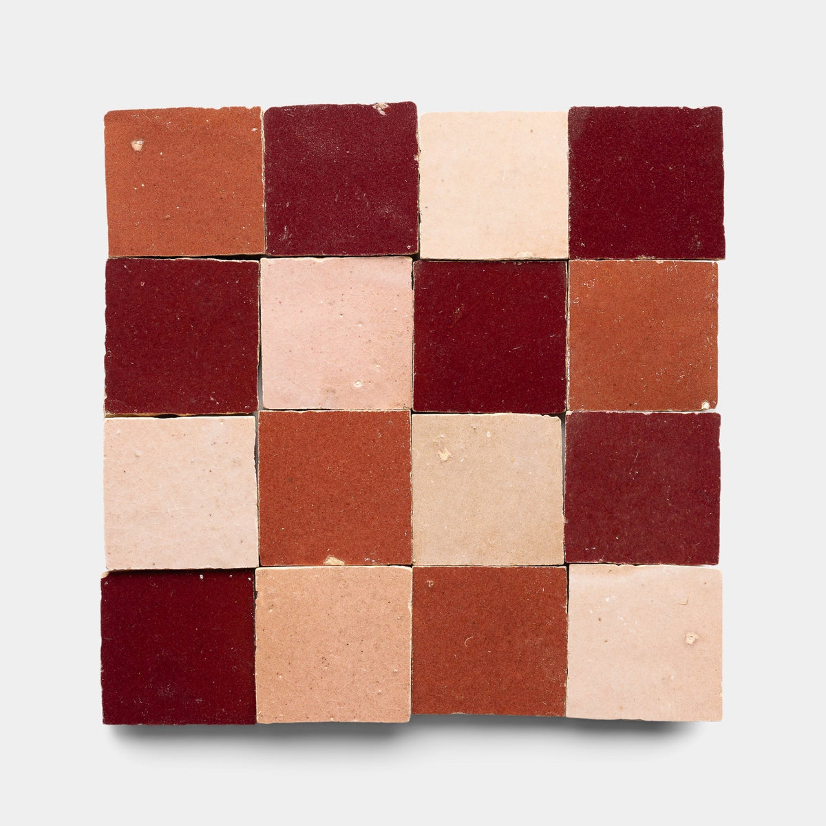 A sample of Zia Tile’s Rouge + Terra Rosa + Desert Bloom Checkerboard features sixteen handmade tiles in a 4x4 square, displaying red, pink, and beige tones on light gray.