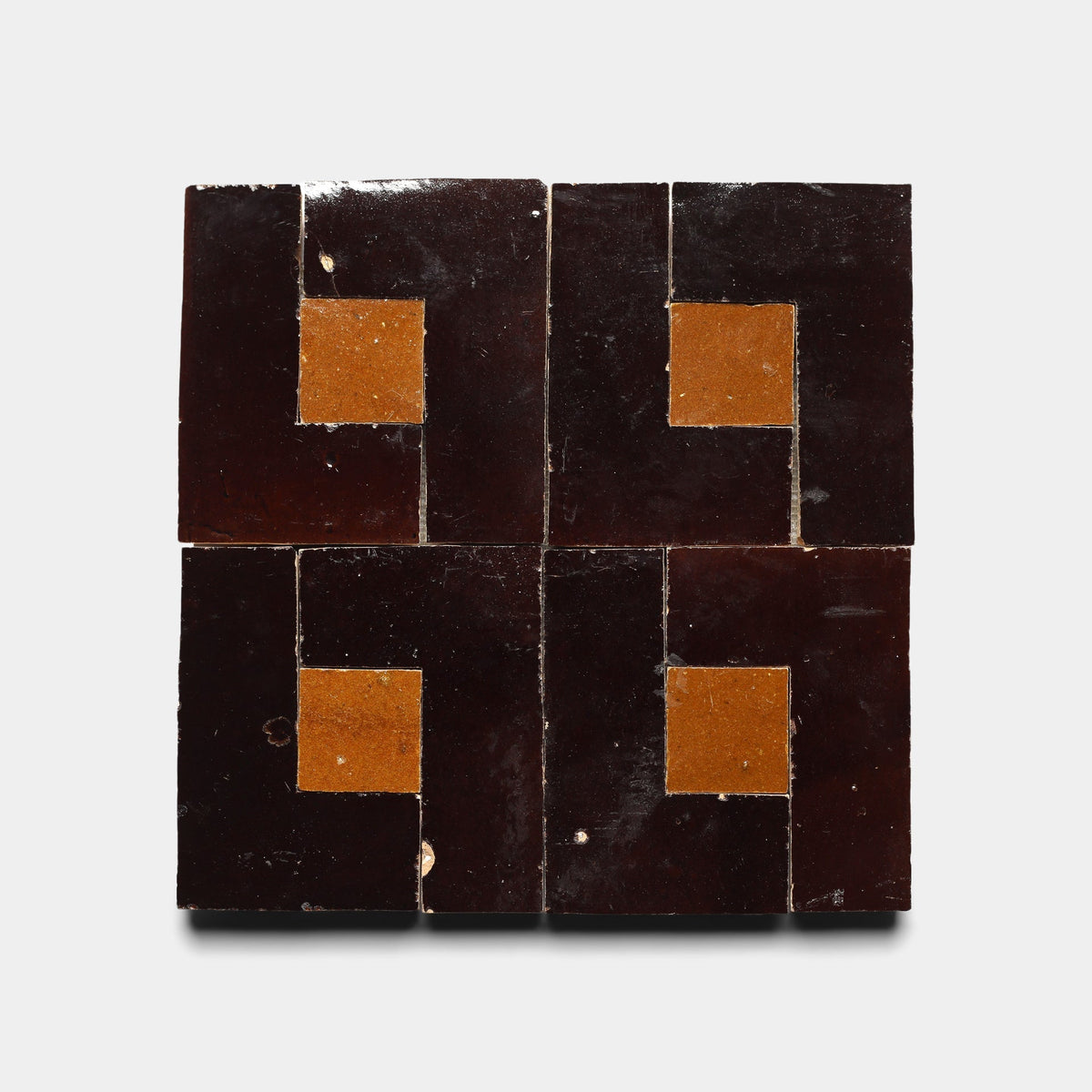 The Rubric 5, Sample by Zia Tile features four handmade tiles in a 2x2 grid, each with a dark brown L-shaped border and an orange-brown center, creating a bold symmetrical geometric pattern.